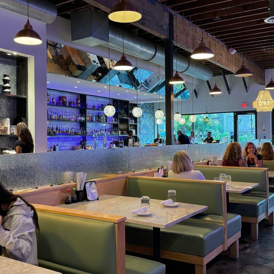 Spacious modern restaurant interior with green booths, occupied tables, pendant lighting, and a blue-lit bar.