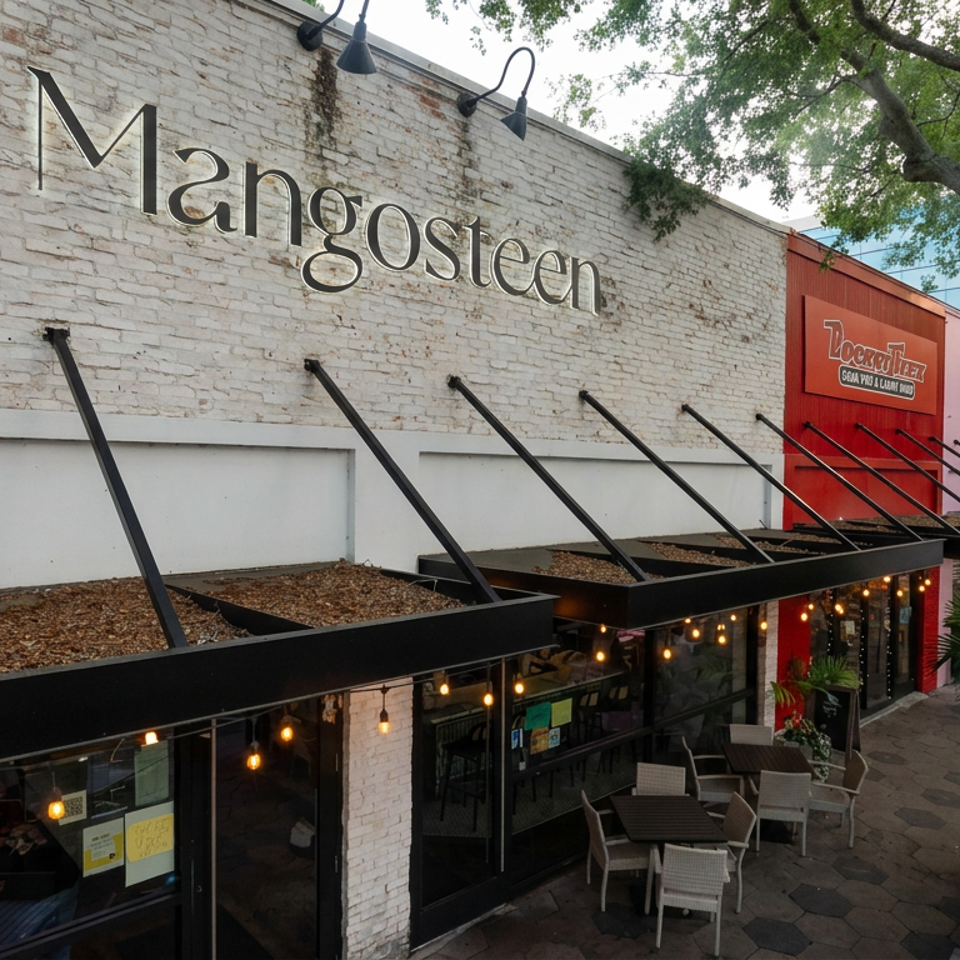 Mangosteen restaurant exterior with white brick walls, outdoor tables, string lights, and tree-lined patio.