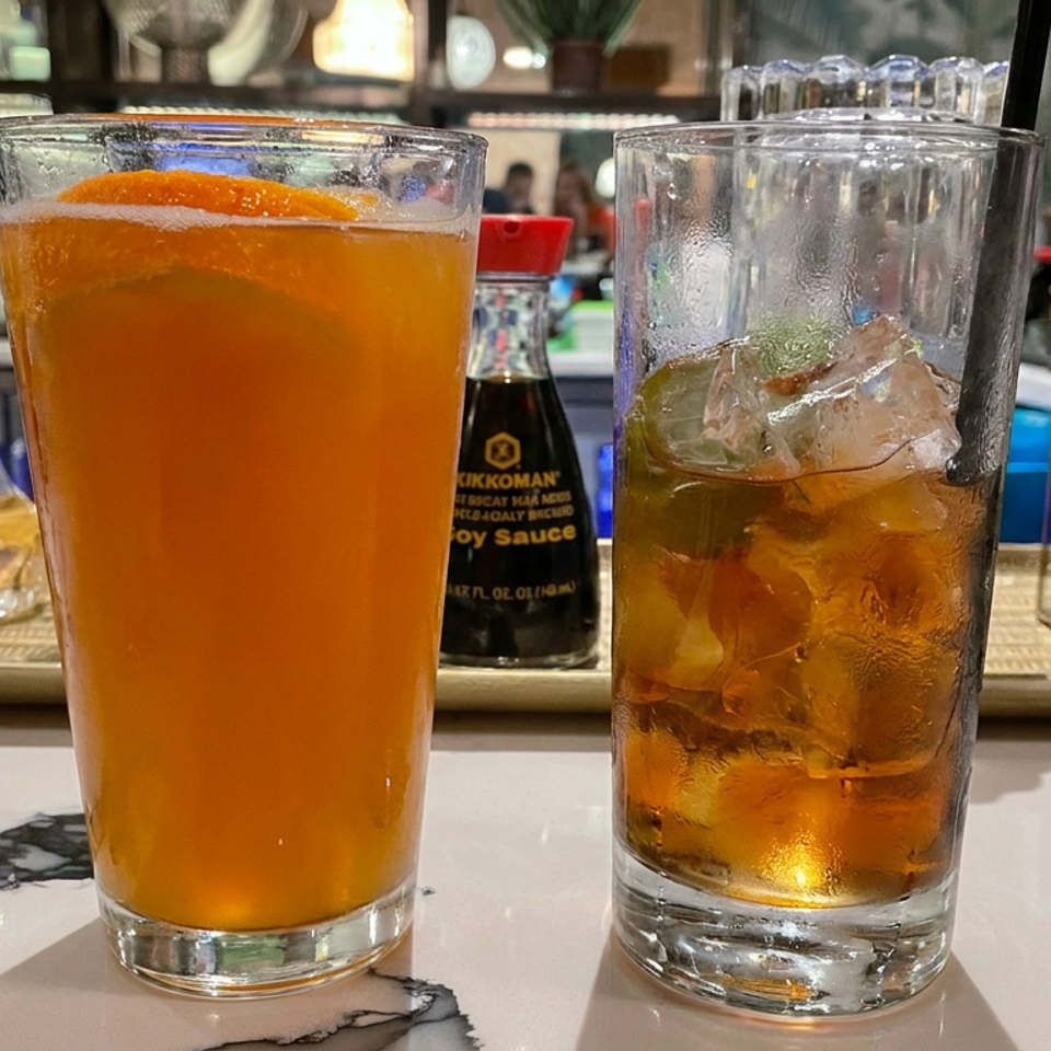 Two amber cocktails, one garnished with citrus and the other with ice, sit on a marble restaurant bar.